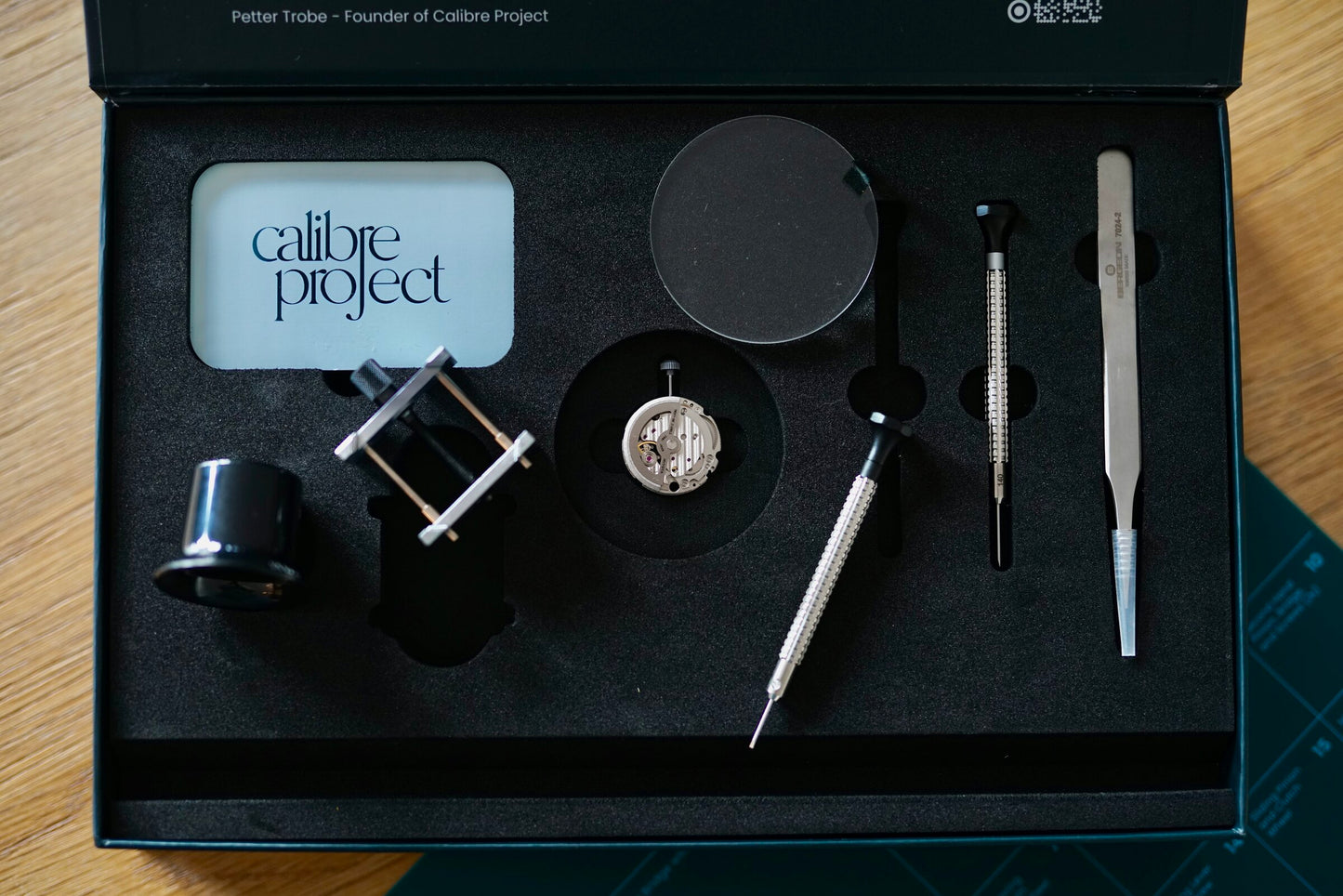 Calibre Learning Kit laid out in its box: the movement, movement holder, loupe, screwdrivers, tweezers and branded card
