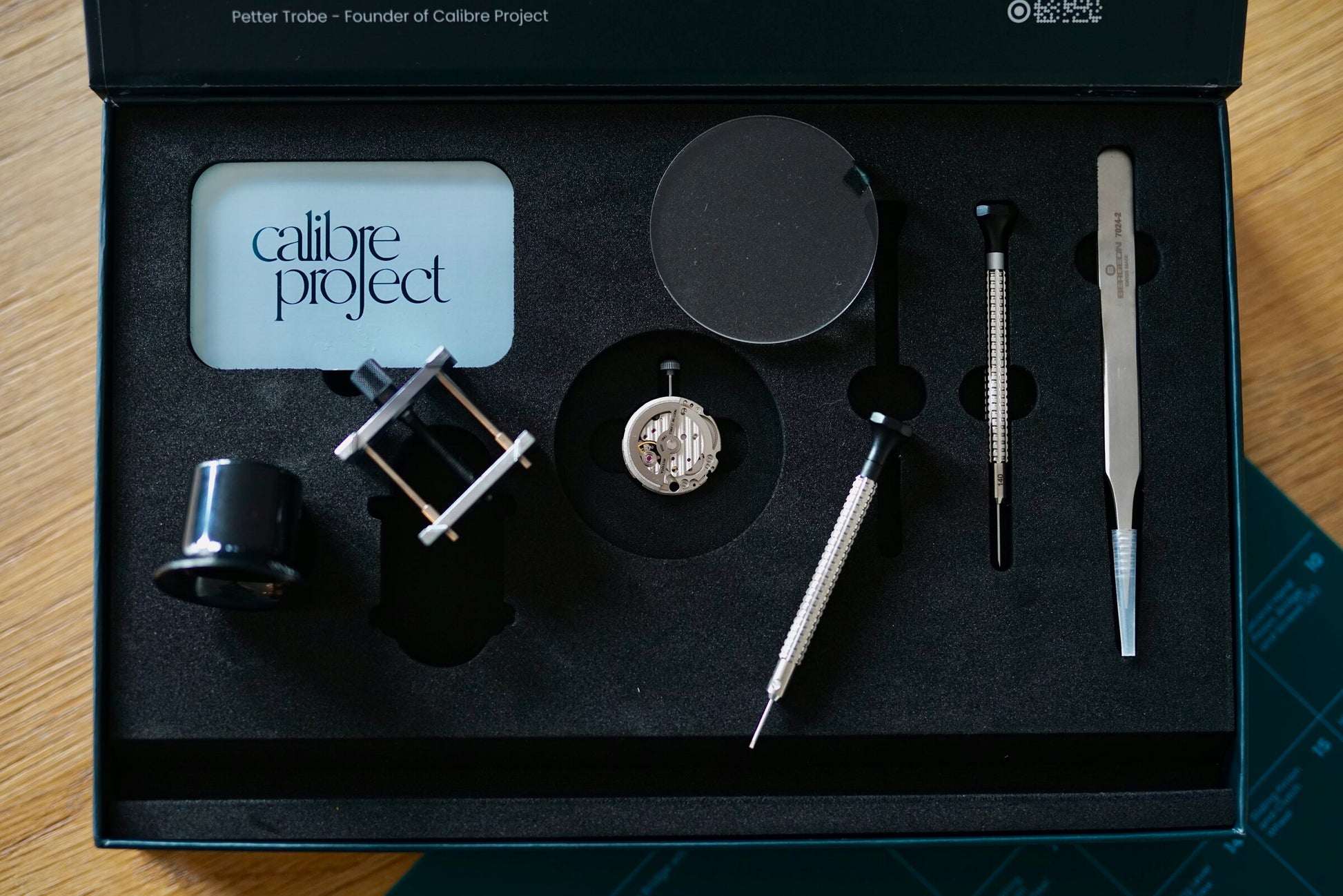 Calibre Learning Kit laid out in its box: the movement, movement holder, loupe, screwdrivers, tweezers and branded card